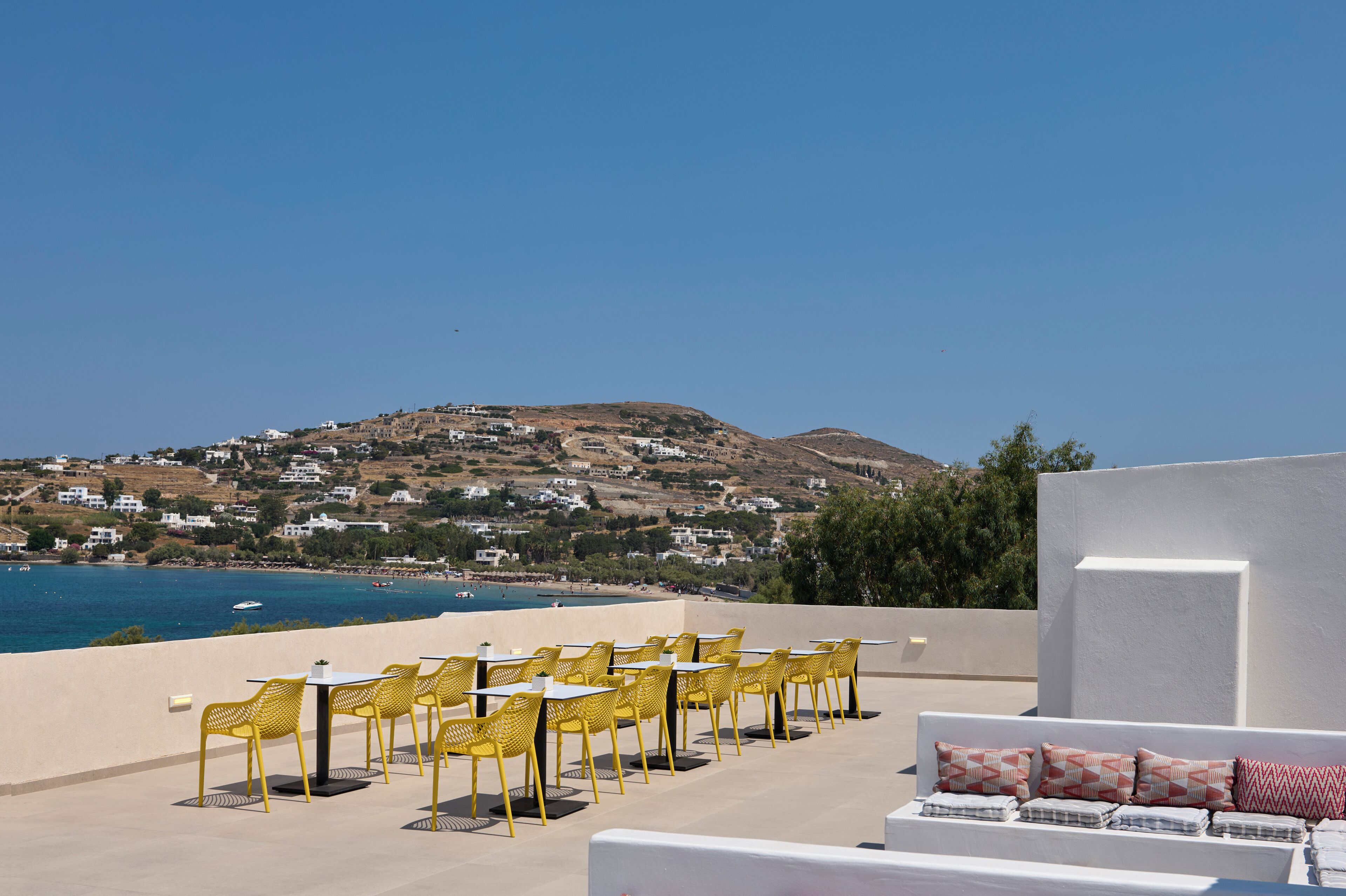 A terrace with yellow chairs and tables overlooking a coastal village.