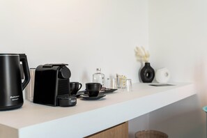 A modern kitchen counter with a coffee maker, cups, and a vase with dried flowers.