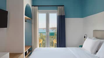A hotel room with a bed, a TV, a desk, a chair, and a view of the sea.