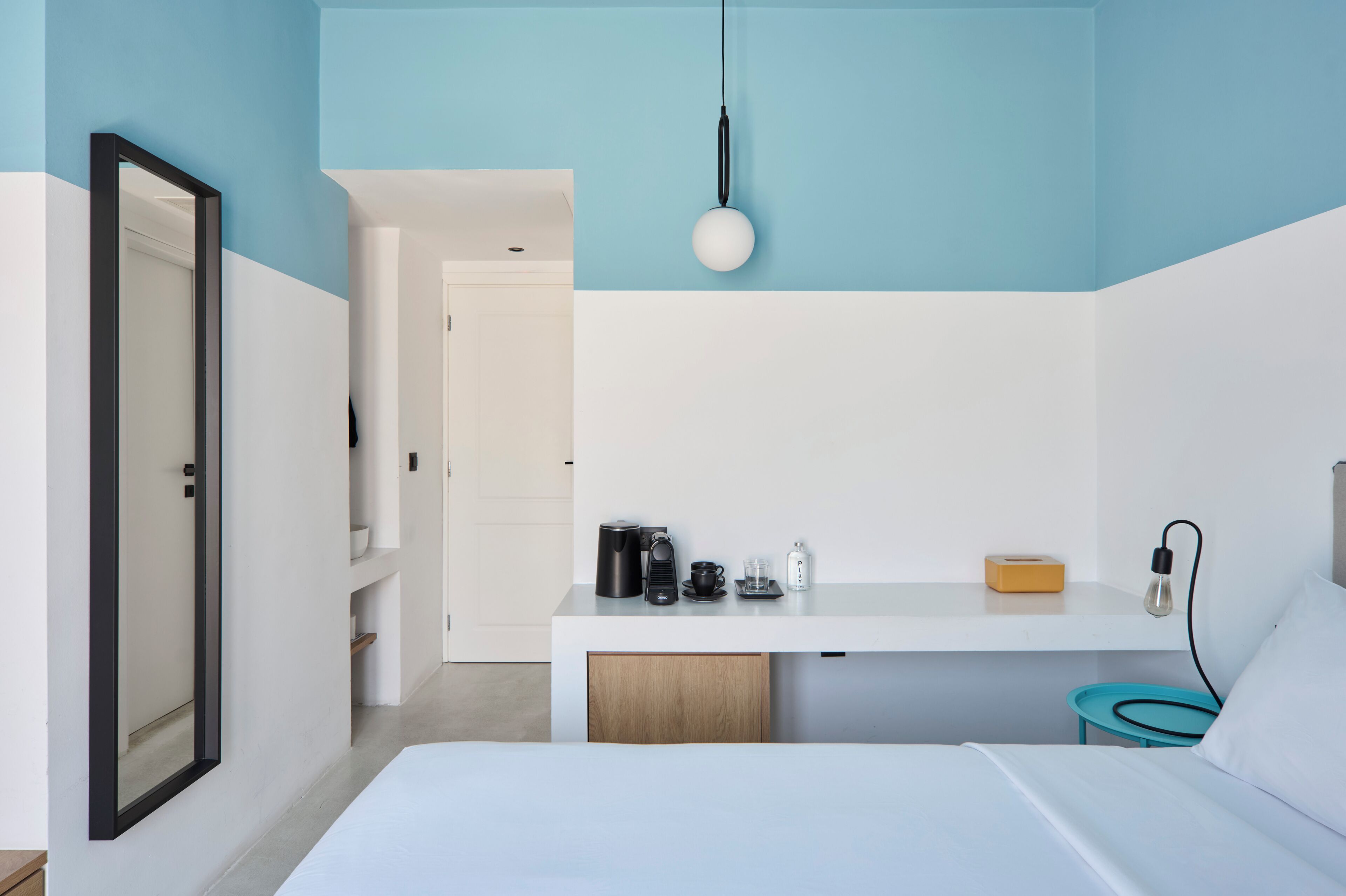 A modern hotel room with a bed, a desk with a coffee maker, a lamp, and a bedside table with a tissue box.