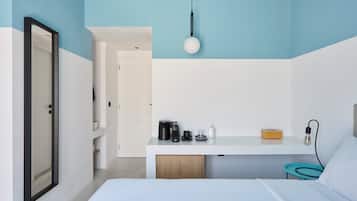 A modern hotel room with a bed, a desk with a coffee maker, a lamp, and a bedside table with a tissue box.