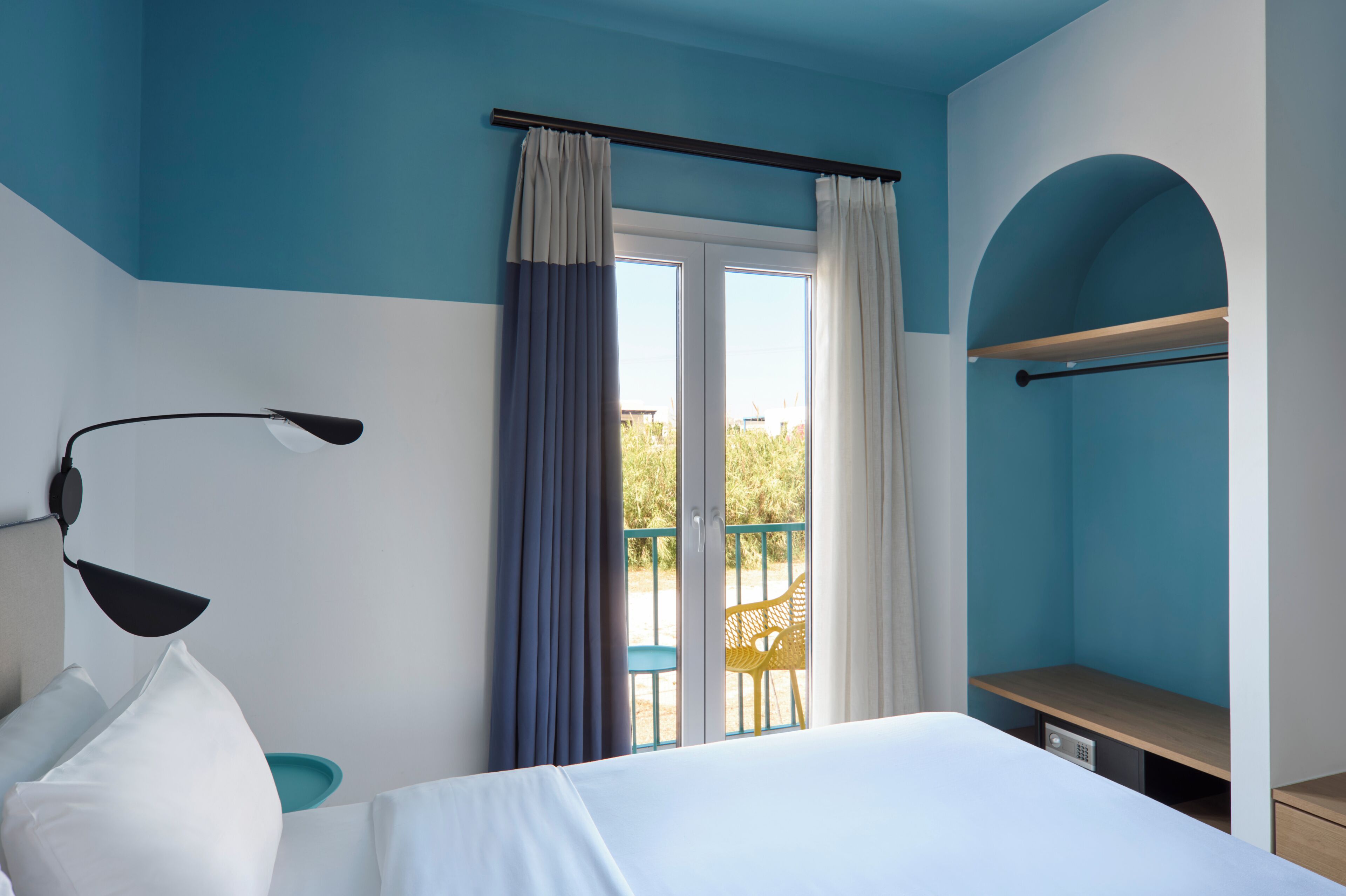 Una habitación de hotel con cama, escritorio, silla, balcón y ventana con cortinas.