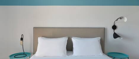 Una cama bien tendida con dos almohadas, cabecero y lámpara de pared.