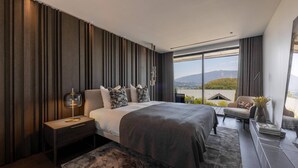 A modern bedroom with a large bed, a nightstand, a chair, and a view of the outdoors. - Villa Tomar (Talloires-Montmin)