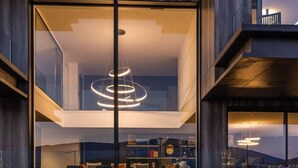 A modern house with large glass windows, a circular light fixture, and a view of the landscape. - Villa Tomar (Talloires-Montmin)