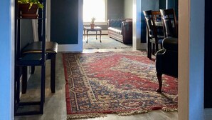 Un salon avec un mur bleu foncé, un plancher en bois, un tapis à motifs et un canapé.