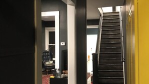 Un couloir avec un escalier menant à un deuxième étage, un fauteuil en cuir noir et une petite table sur laquelle sont posés divers objets.