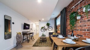 Een moderne woonkamer met een bakstenen muur, een opgehangen fiets, een eettafel voor vier personen en een televisie aan de muur.