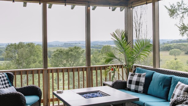 Un espacio de estar al aire libre con techo, amueblado con sillas de mimbre, una mesa y un ventilador de techo.