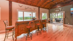 Una habitación amplia con techo de madera, una zona de bar con taburetes y grandes ventanales que ofrecen vistas al exterior.