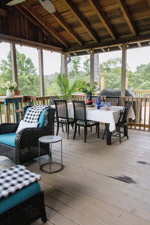 Eine überdachte Terrasse im Freien mit Esstisch, Korbmöbeln und Blick ins umliegende Grün.