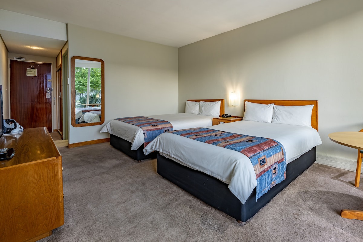 A hotel room with two beds, a desk, a chair, and a small table.