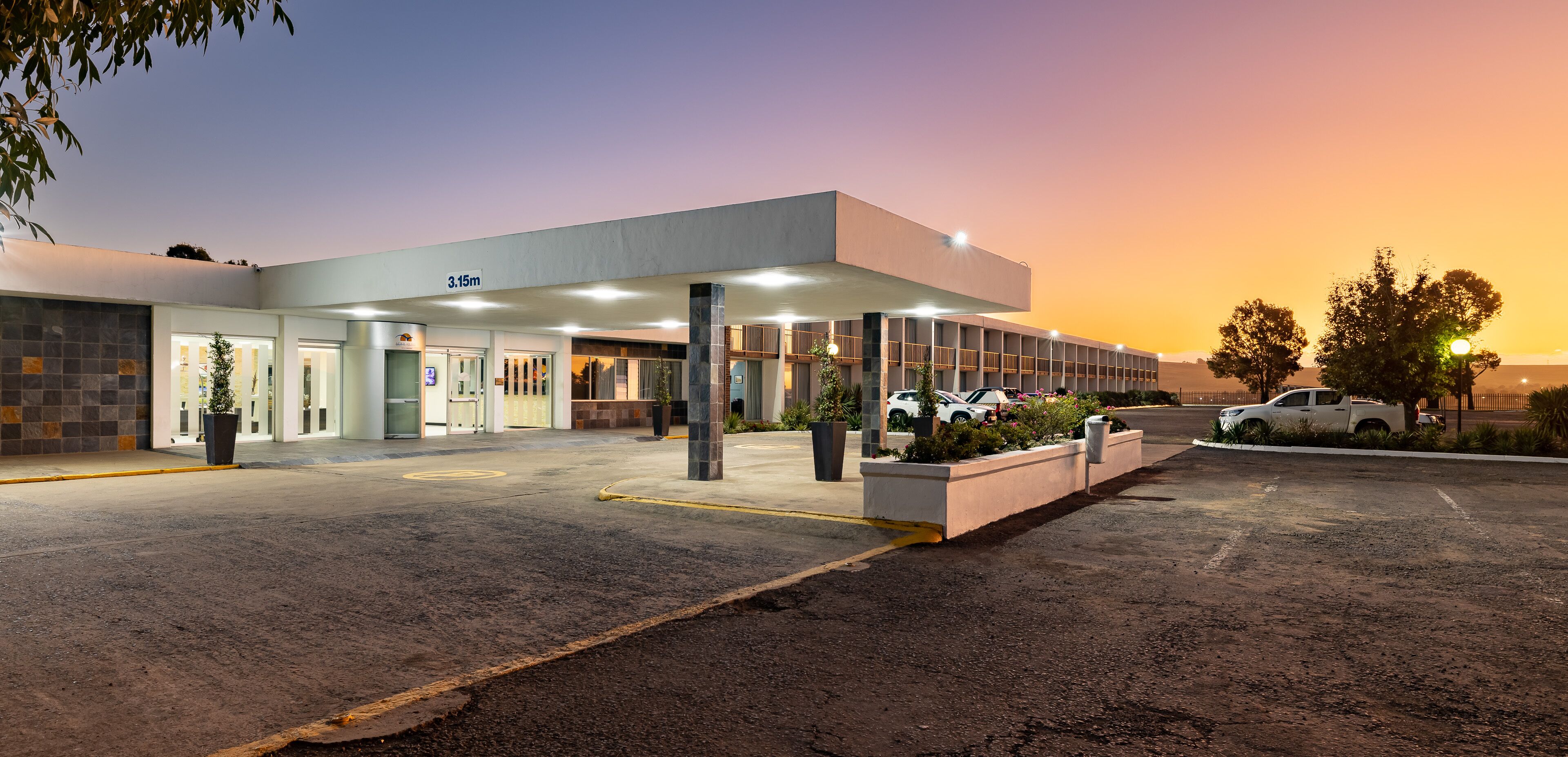 A modern building with a covered entrance, outdoor seating, and a parking area.