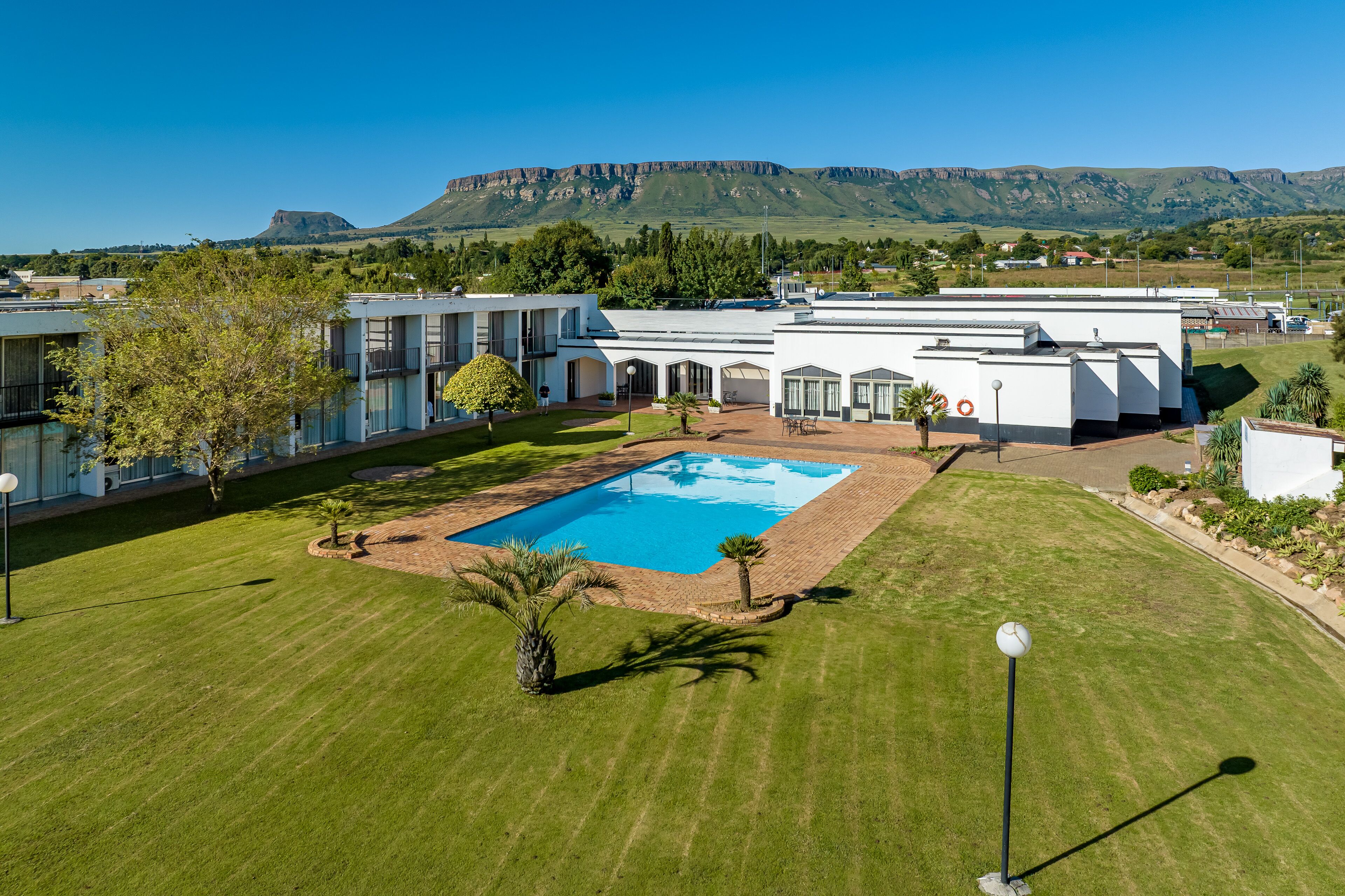 A modern hotel with a swimming pool, surrounded by well-maintained lawns and palm trees.