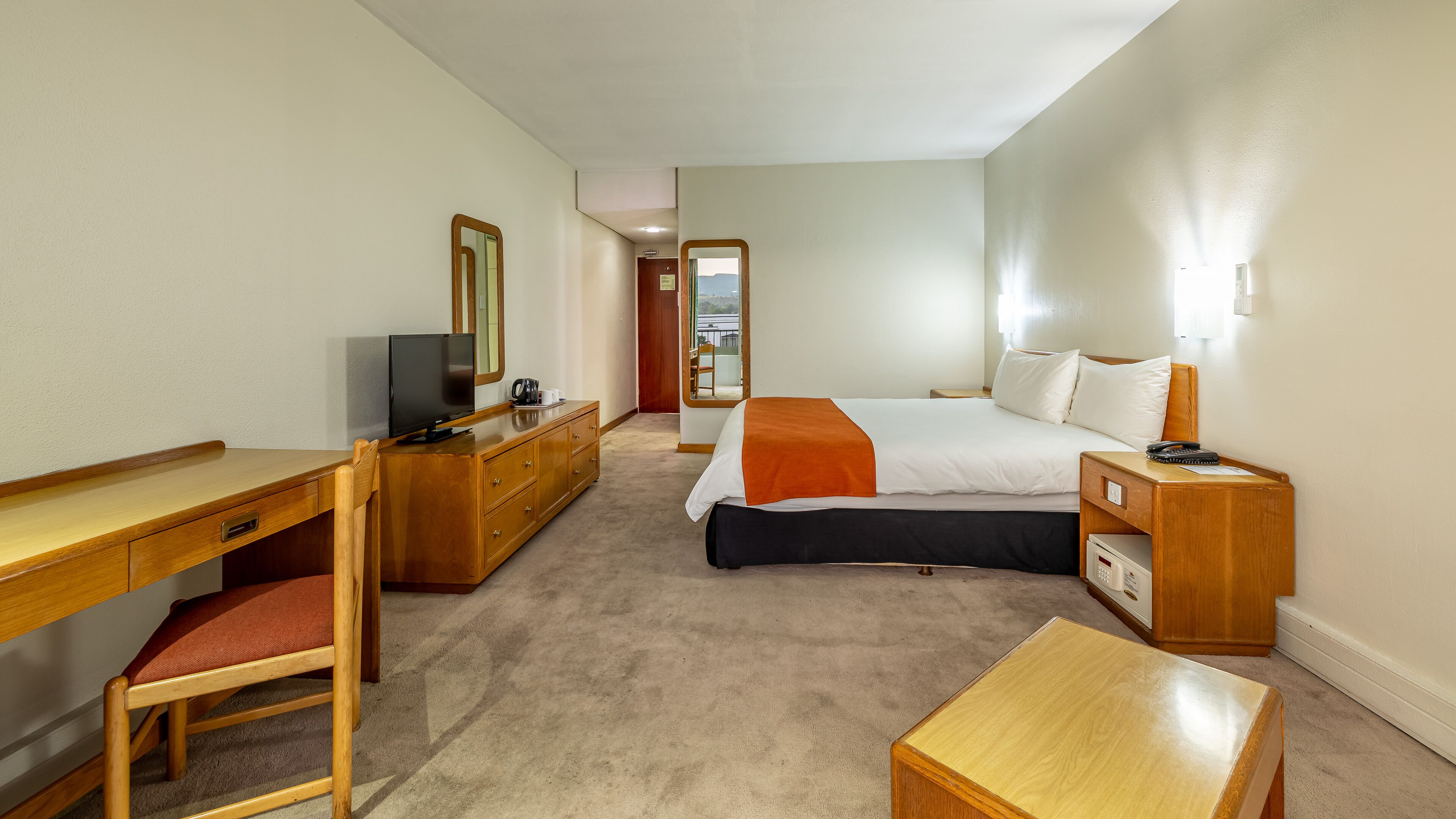 A hotel room with a bed, a desk, a chair, a TV, and a bedside table.