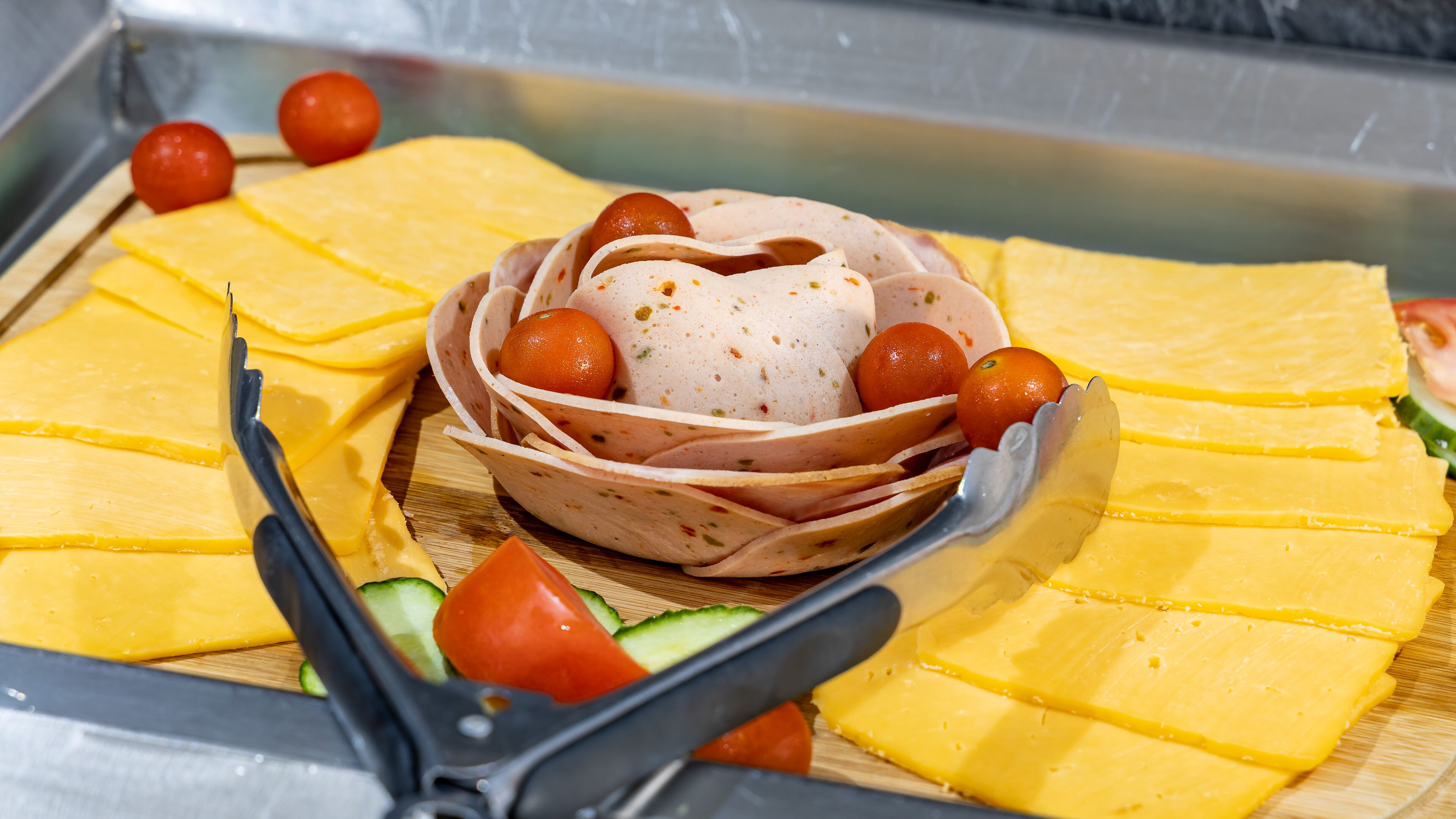 A buffet with sliced yellow cheese, a bowl of meat with herbs, and cherry tomatoes.