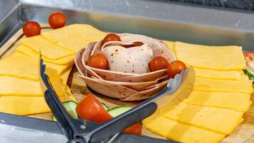 A buffet with sliced yellow cheese, a bowl of meat with herbs, and cherry tomatoes.