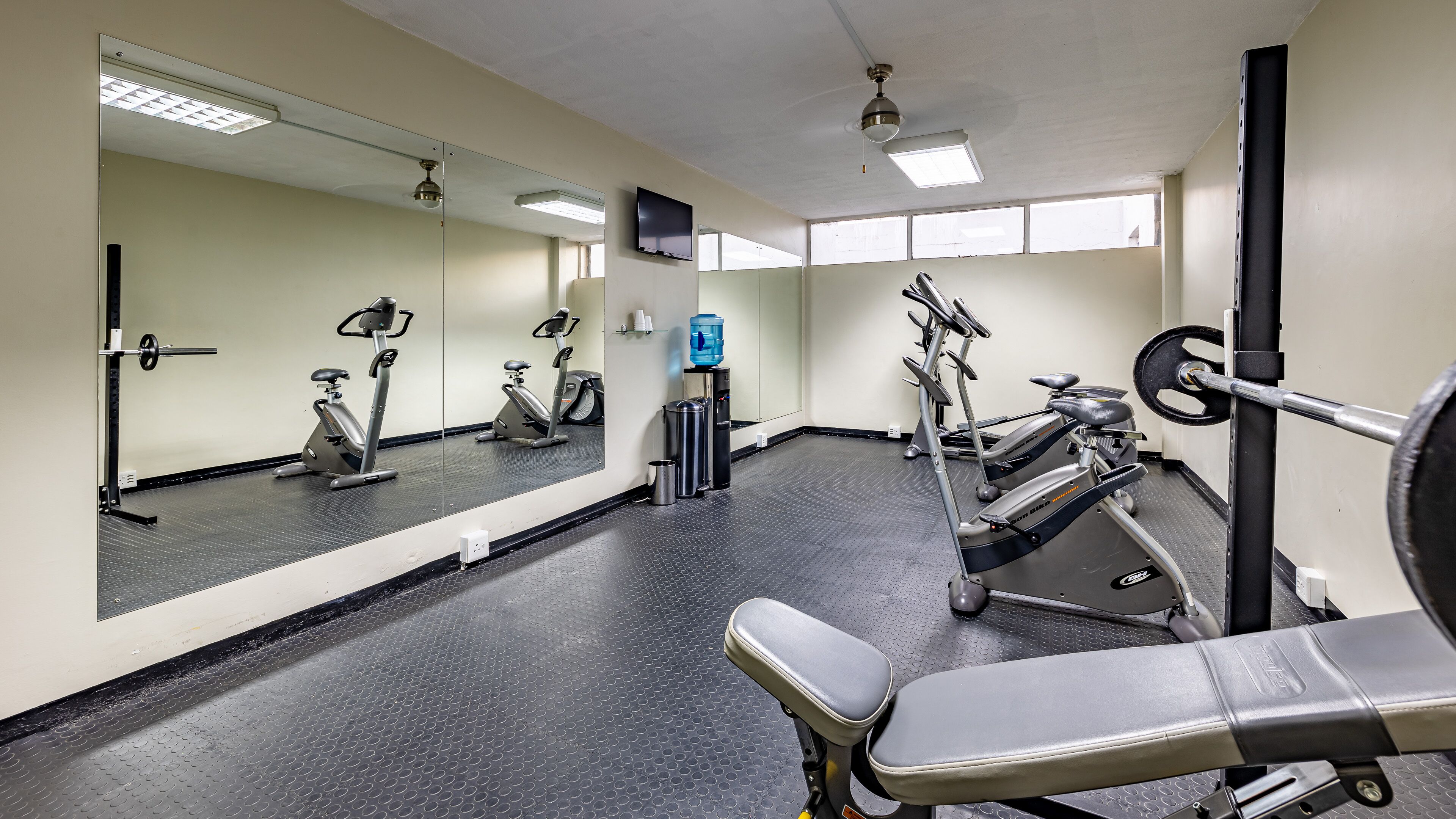 A gym with exercise equipment, a water dispenser, and a mirror.