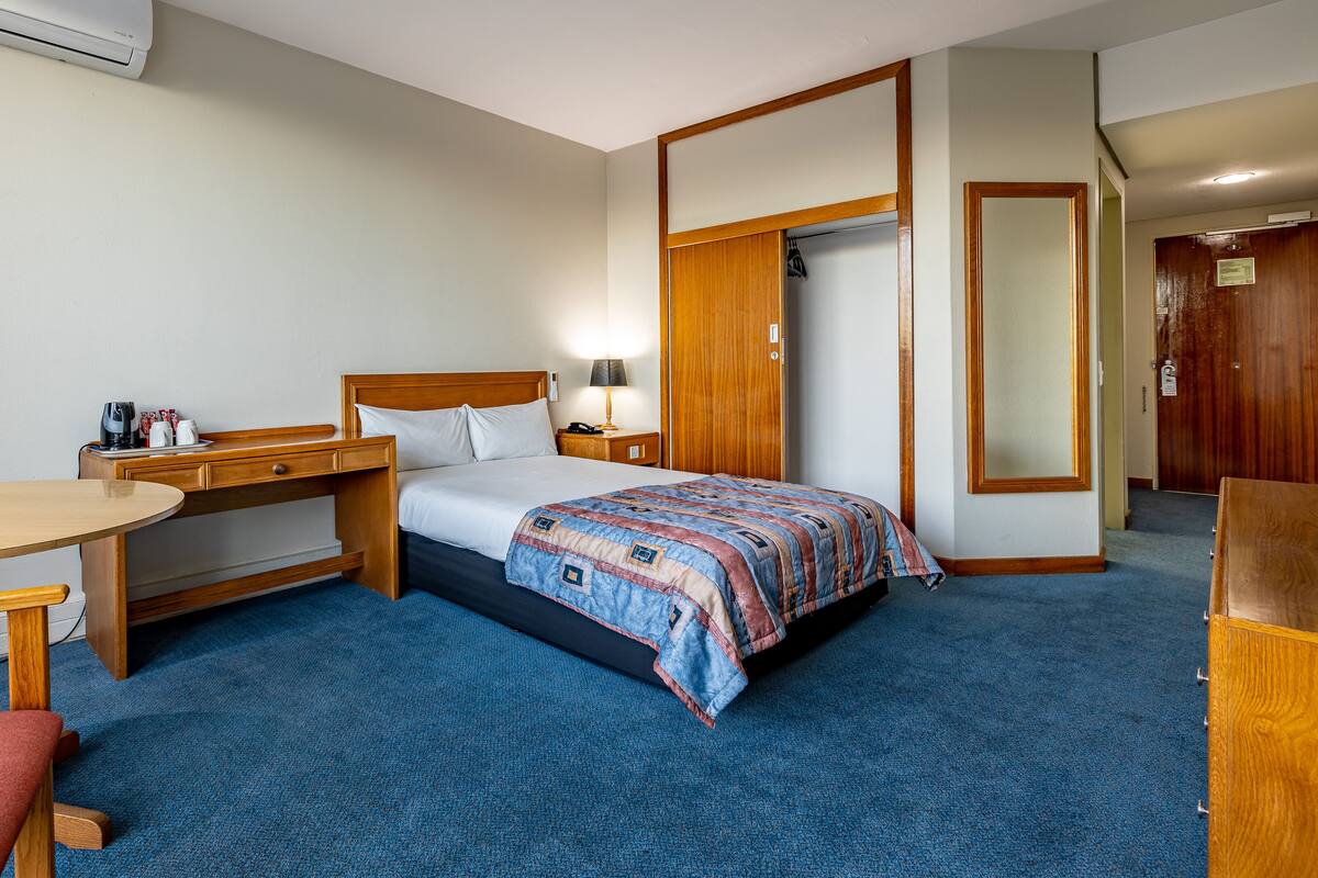 A hotel room with a bed, a desk, a chair, a lamp, and a wardrobe.