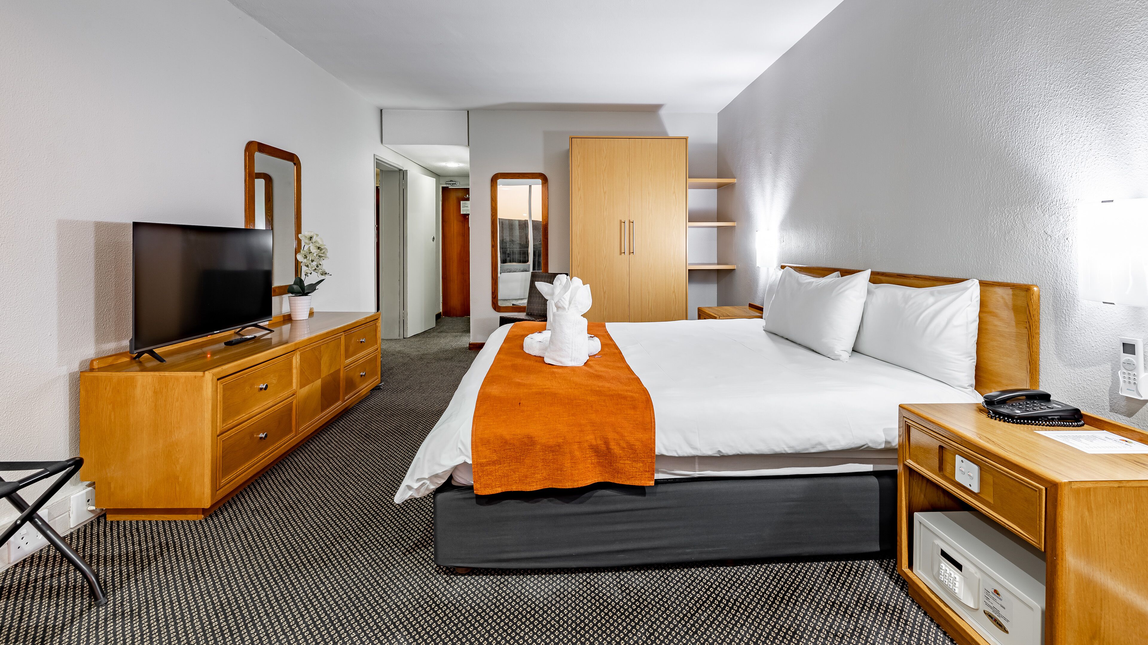 A hotel room with a bed, a TV, a wooden dresser, a desk with a phone, and a microwave.