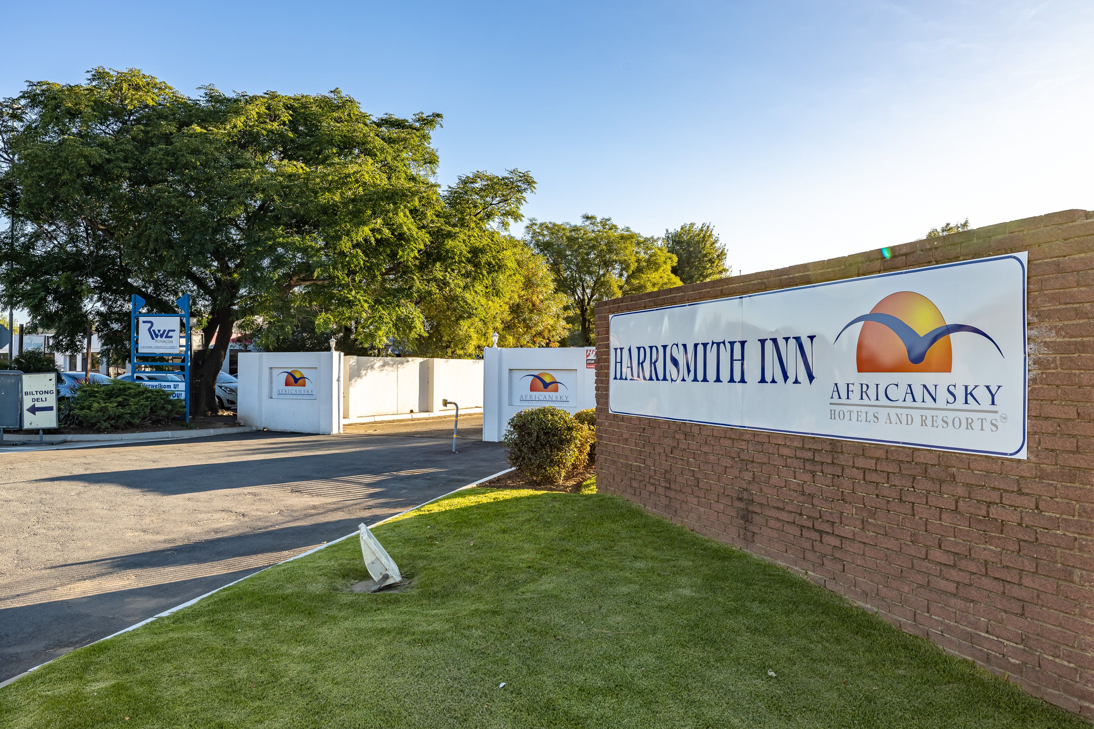 Señal de HARRISMITT INN AFRICANSKY HOTELS AND RESORTS con un logotipo, una pared de ladrillo y una zona ajardinada.