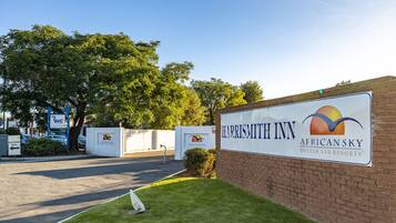 Señal de HARRISMITT INN AFRICANSKY HOTELS AND RESORTS con un logotipo, una pared de ladrillo y una zona ajardinada.