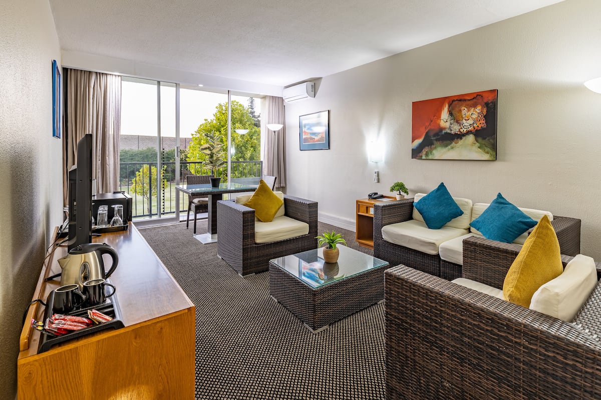 A modern hotel room with a balcony, wicker furniture, a glass coffee table, and a painting of a lion.