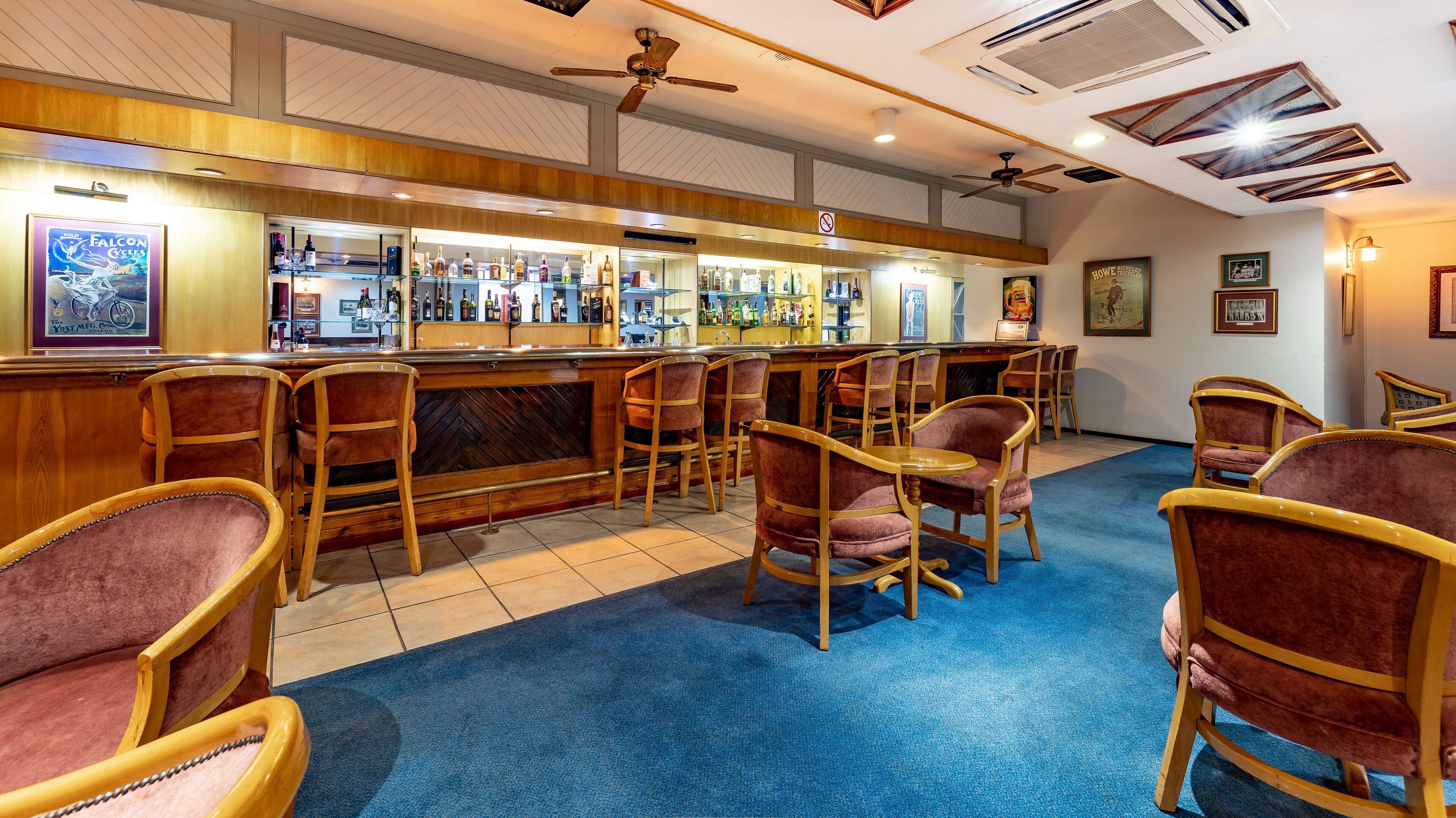 Una zona de bar con mostradores de madera, varios taburetes y un suelo cubierto de moqueta azul.