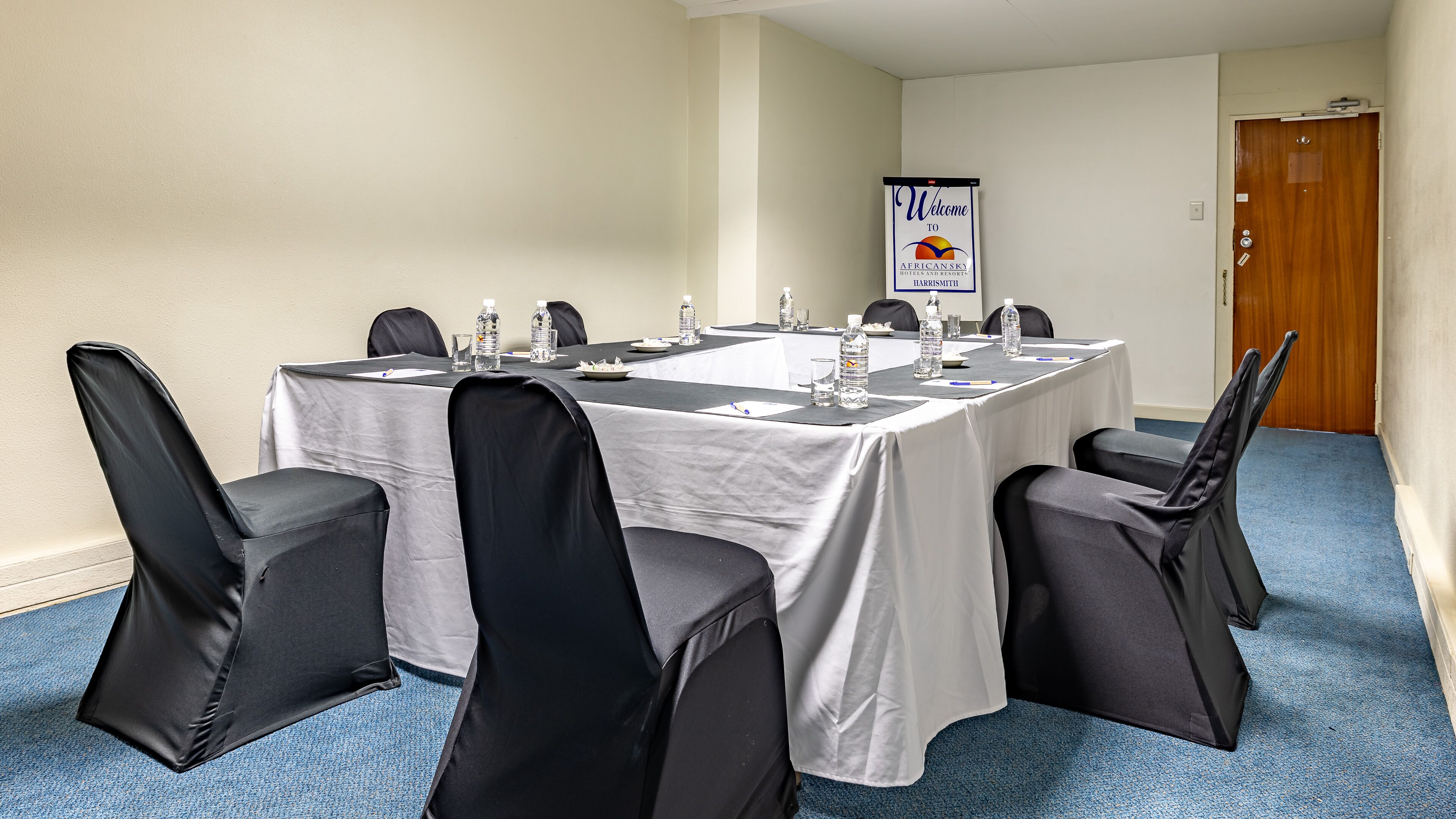 A conference room with a long table, black chairs, water bottles, and a welcome sign for African Sky Hotels and Resorts.