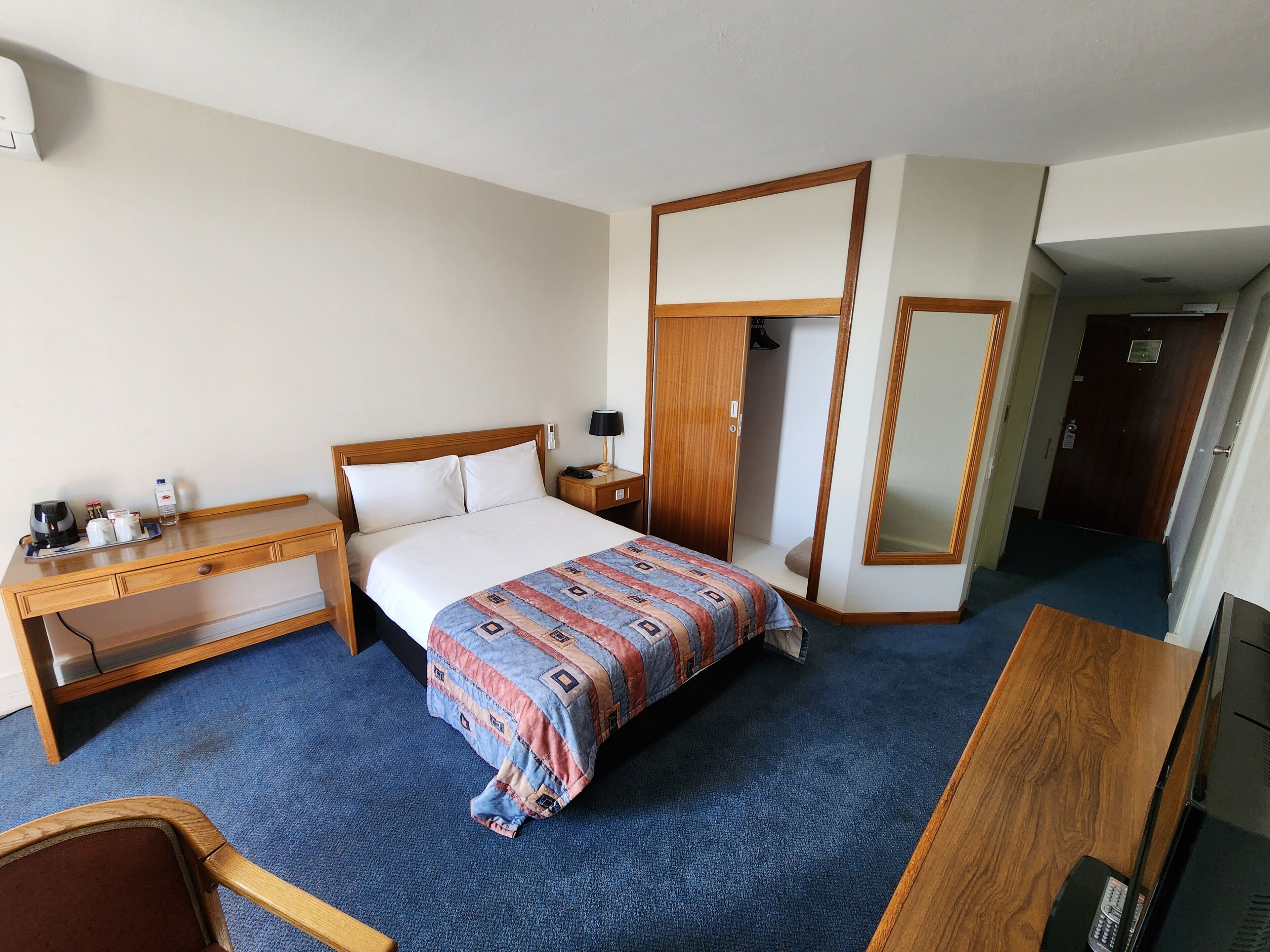 Habitación de hotel con cama, escritorio, armario y espejo.