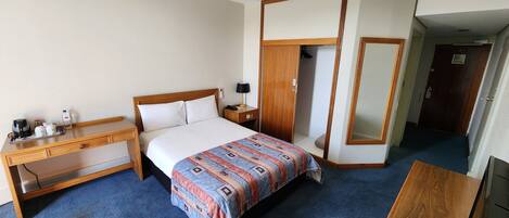 Habitación de hotel con cama, escritorio, armario y espejo.