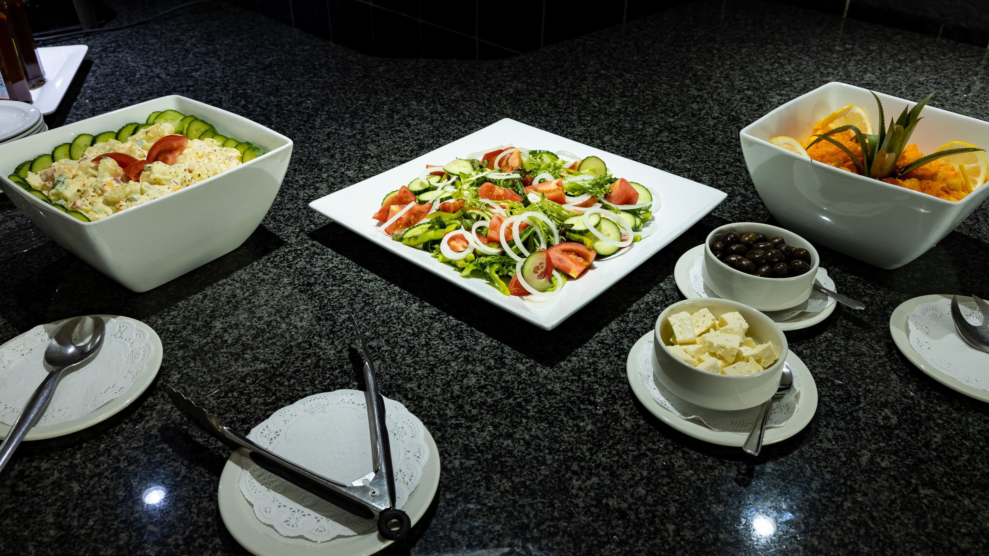 Una mesa de comedor con diversos platos, incluyendo una ensalada, un cuenco de aceitunas y un cuenco de queso feta.