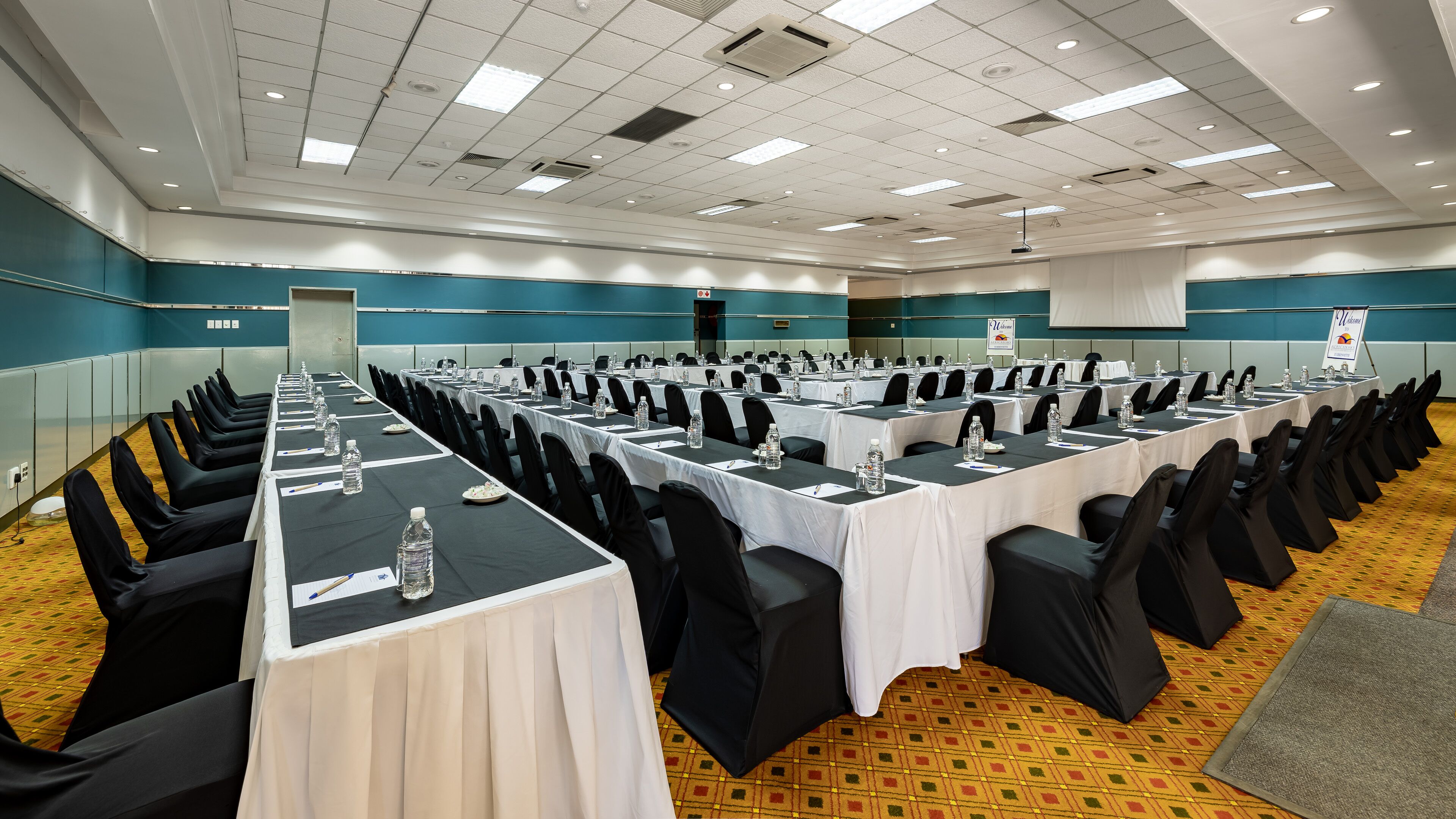 Un salón de conferencias con filas de mesas, sillas y botellas de agua, con una decoración en colores azul y blanco.