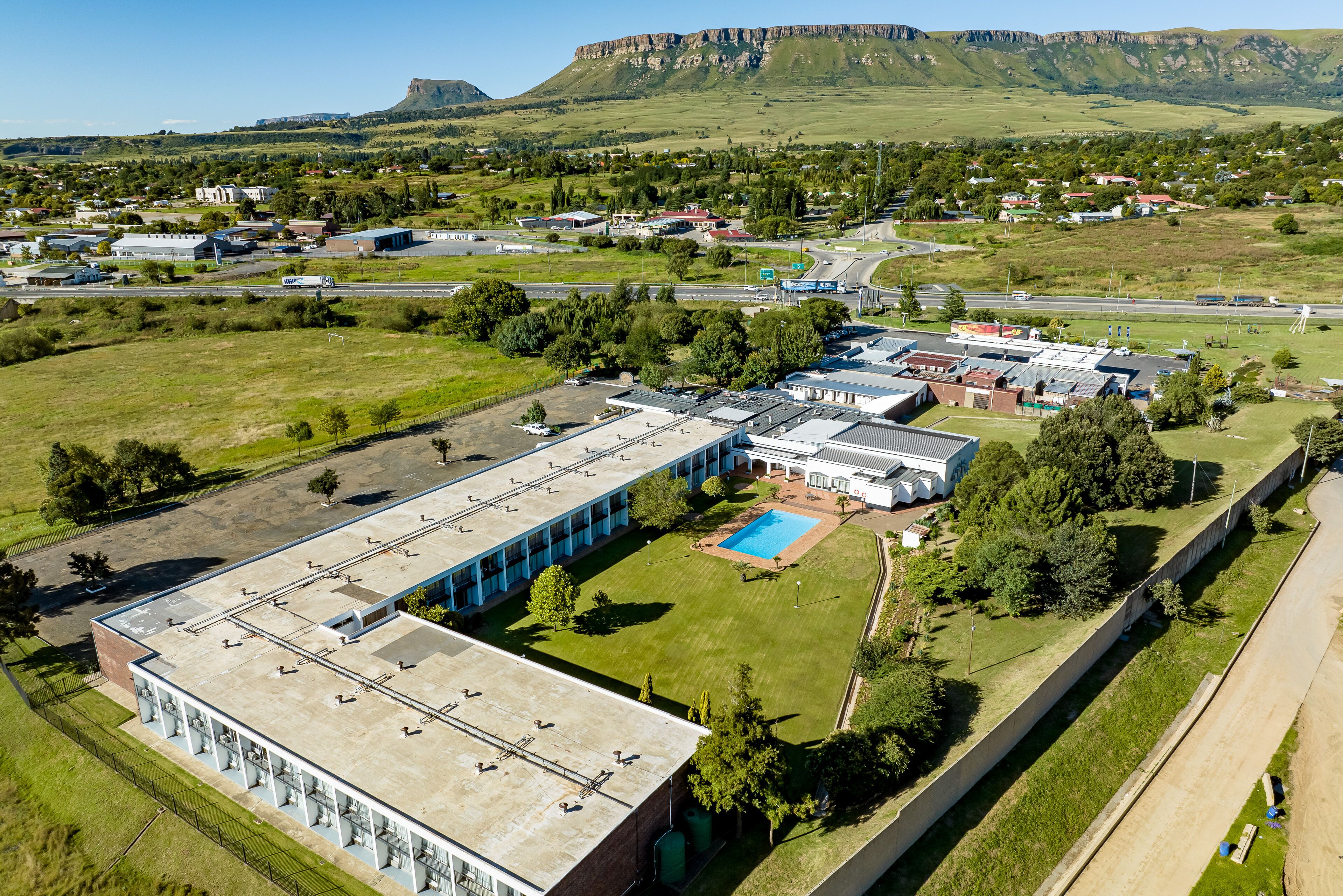 An industrial building with a large parking lot, a swimming pool, and a view of a mountainous landscape.