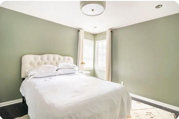 Una cama bien tendida con sábanas blancas en una habitación con paredes verde claro y techo blanco.