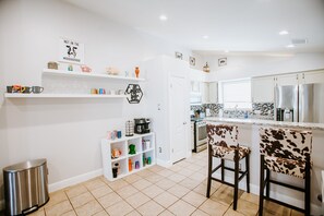Une cuisine moderne avec des meubles blancs, un coin café et un dosseret carrelé.