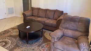 Un salón con un sofá de cuero marrón, un sillón a juego y una pequeña mesa redonda de centro.