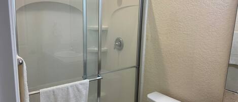A bathroom with a glass-enclosed shower, a white toilet, and a beige wall.