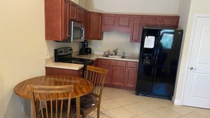 Una cocina compacta con armarios de madera, un refrigerador negro, un microondas, una estufa y un lavamanos. Hay una mesa de comedor de madera con sillas.