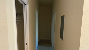 Un pasillo estrecho con suelo de baldosas, una puerta blanca a la izquierda y un interruptor de luz en la pared.