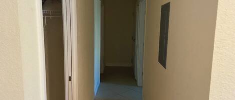 Un pasillo estrecho con suelo de baldosas, una puerta blanca a la izquierda y un interruptor de luz en la pared.