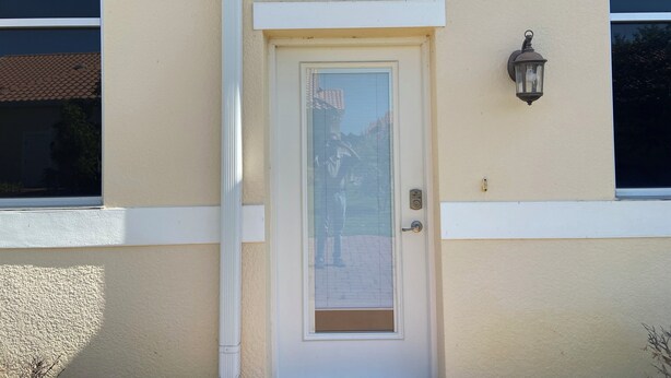 Un edificio color beige con una puerta blanca, una ventana con persianas y un farol fijado a la pared.