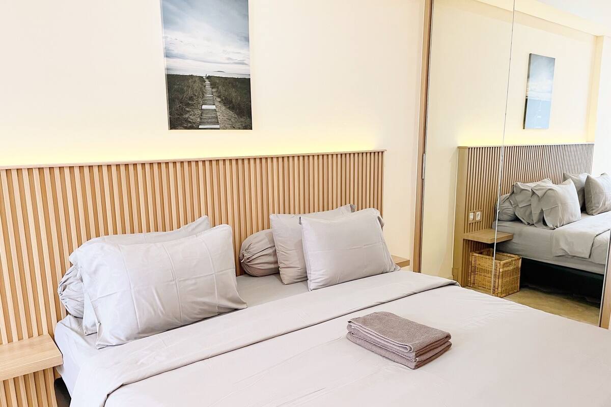 A modern bedroom with a wooden headboard, a bed with white linens, and a small bedside table with a lamp.
