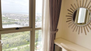 Una habitación con un ventanal amplio que da a una vista urbana, un espejo con reflejo de sol en la pared y una consola blanca.