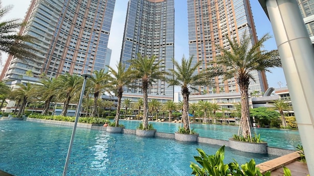Un moderno complejo residencial con edificios altos, una piscina y palmeras.