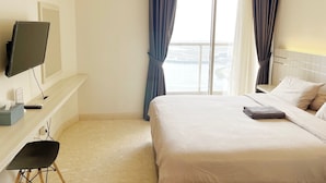 Habitación de hotel con cama, televisor montado en la pared, escritorio con silla y ventana con cortinas.