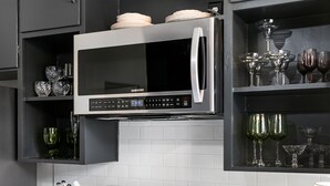 Una cocina moderna con muebles oscuros, un microondas de acero inoxidable y una estufa a gas.
