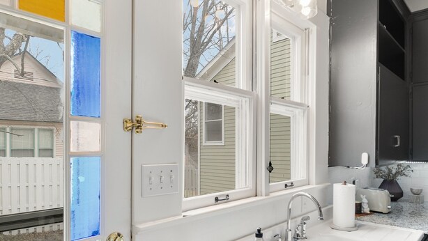 Una cocina con puerta blanca, ventana, lavamanos y armarios.