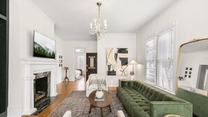 Un salón amplio con un sofá verde, una chimenea, un candelabro y obras de arte en las paredes.