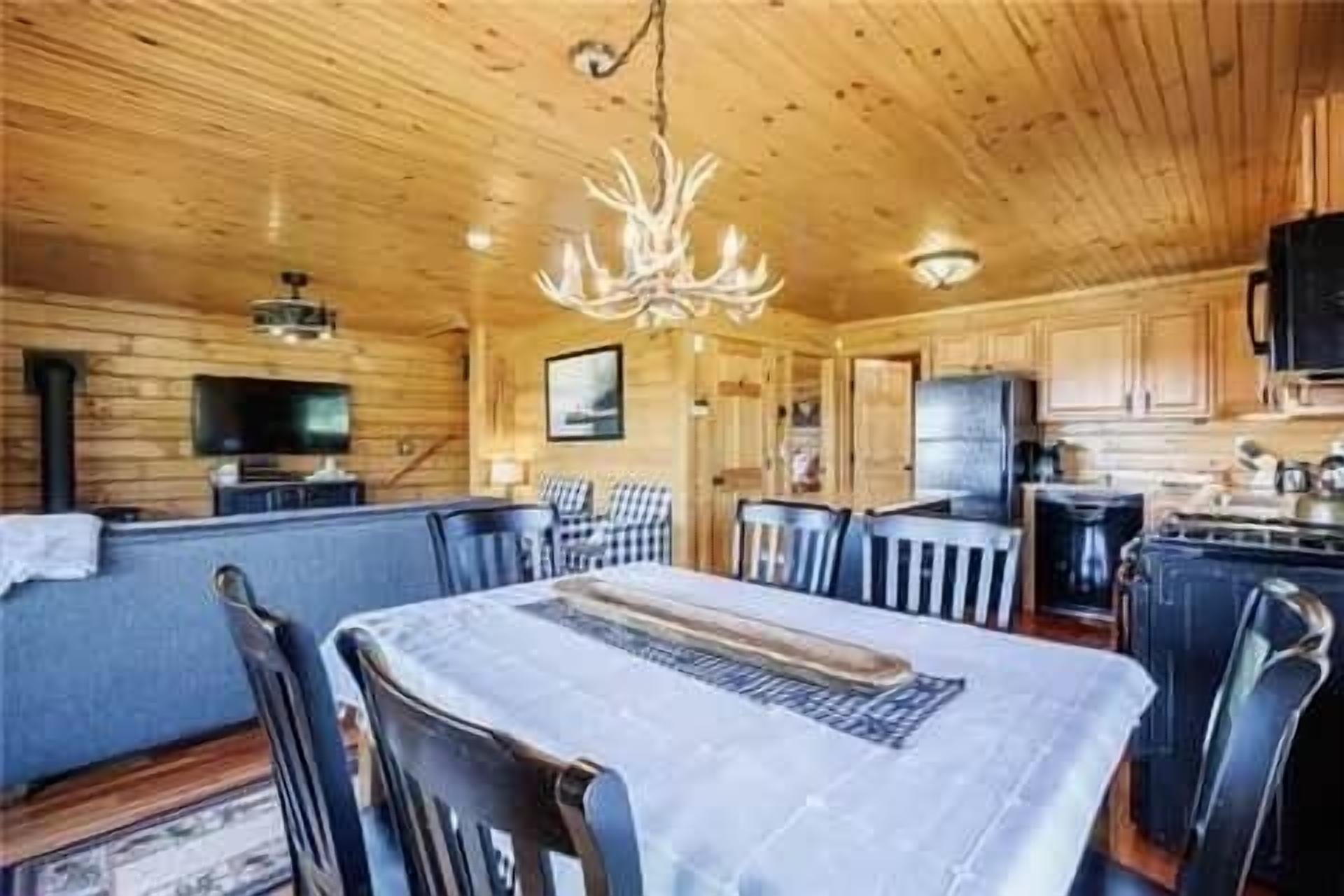 Interior de una cabaña de madera con comedor, cocina y una gran lámpara de araña.
